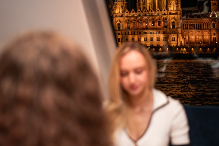 Two people dining indoors with a view of a lit Gothic building at night through the window.