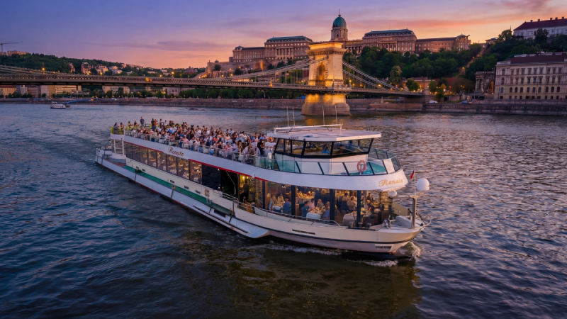 River cruise ship on water at sunset with historic bridge and buildings in background.