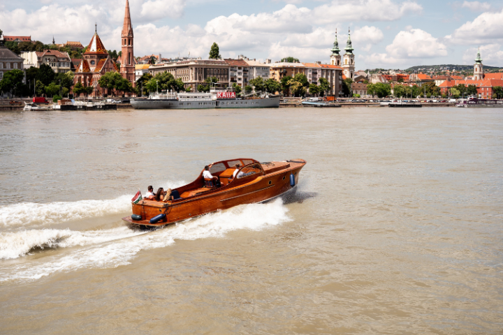 Wooden boat sailing on a river with a cityscape in the background.
