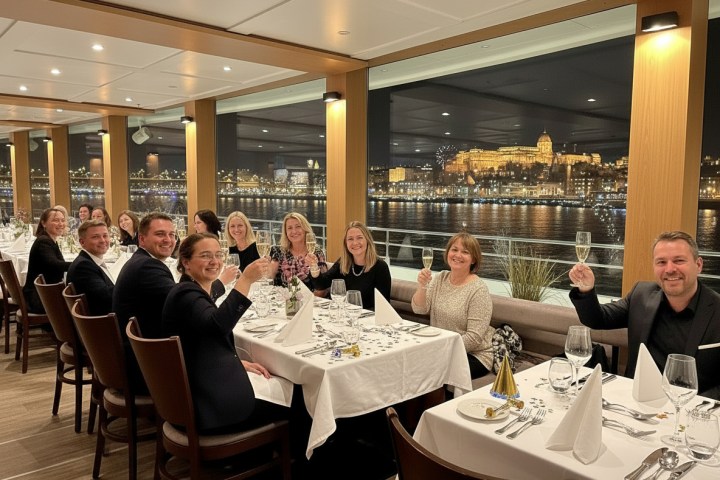 Group of people raising glasses at a long dining table with a cityscape view outside.