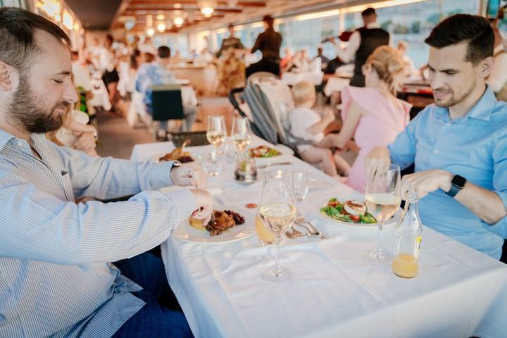 Two men dining with wine in a busy restaurant; background blurred.