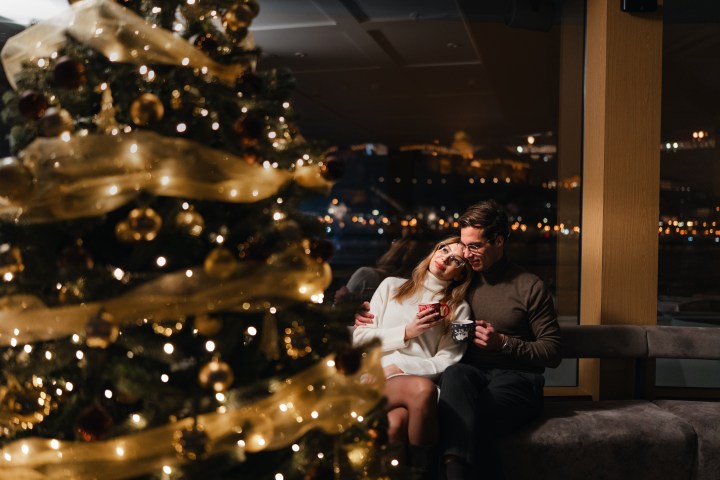 Couple sitting near a decorated Christmas tree, gazing at each other.