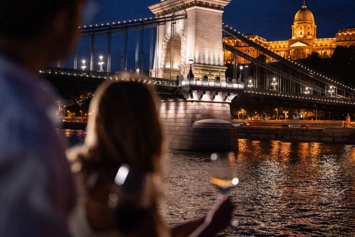 People on a boat at night with a bridge and illuminated building in the background.