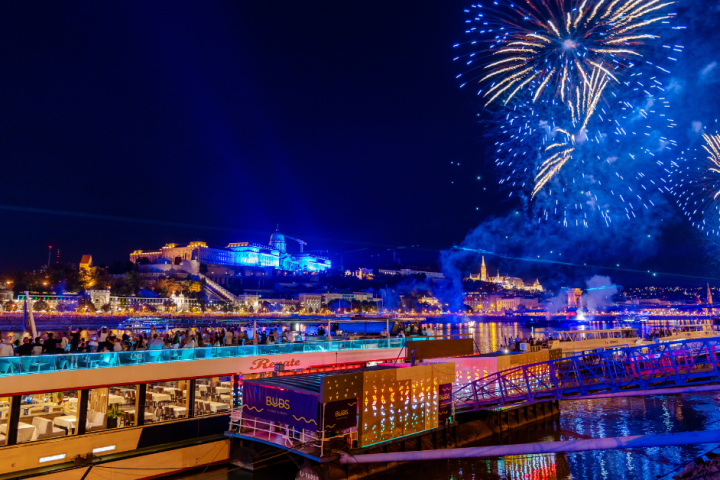 Riverfront fireworks and illuminated buildings at night.
