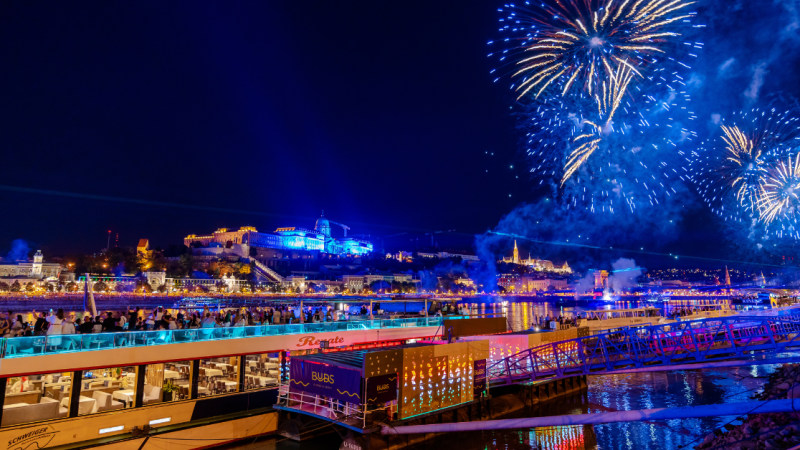 Riverfront fireworks and illuminated buildings at night.