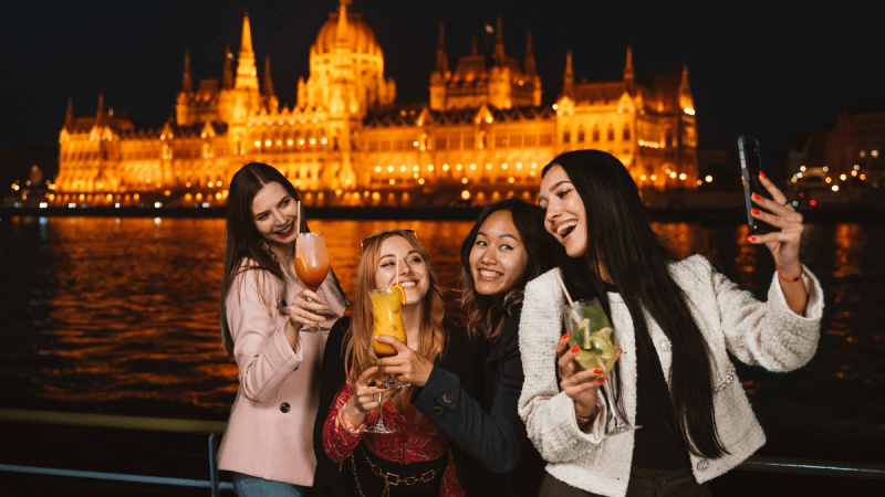 Four people taking a selfie at night with a lit building in the background.