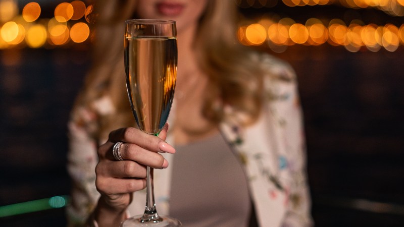 Woman holding a glass of champagne in front of bokeh city lights at night.